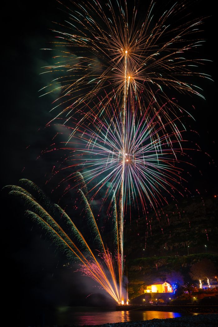 A vibrant firework show illuminates the night sky with reflections on the water.
